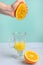 Light background, girl crushes an orange with her hand while receiving juice in a transparent glass