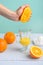 Light background, girl crushes an orange with her hand while receiving juice in a transparent glass