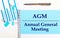 On a light background - light blue diagrams, paper clips and a sheet of paper with the text AGM Annual General Meeting. View from
