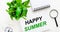 On a light background, there is a white alarm clock, a magnifying glass, a green plant and a notebook with the words HAPPY SUMMER
