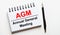 On a light background, a white notebook with are words AGM Annual General Meeting and a pen