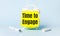 On a light blue background - a white handle and an alarm clock with a bright yellow sticker glued to it with the text TIME TO