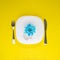 Light blue flower on a plate with silverware. Spring healthy food concept. Vibrant yellow background. Flat lay nature food