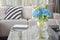 Light blue flower and wine glasses on center table with striped black and white pillow and gray tone pillows on beige sofa