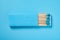 A light blue matchbox and light blue match sticks on a light blue background