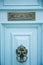 Light blue wooden entrance door with ornated sign and knocker