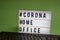 Light box with the inscription: #CORONA HOME OFFICE is behind a black computer keyboard against a green background