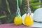 Light Bulb Glass Bottles with Freshly Pressed Orange Tropical Fruits Juice Straw Hat Green Palm Tree Leaves Foliage Background