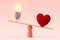 Light bulb and heart on scale on pink background - Concept of woman and love priority over brain in life