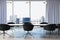 Light conference table surrounded by black chairs on concrete floor in spacious meeting cabinet with city skyline view from