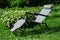 A light folding chair for outdoor recreation stands on the grass next to a flowerbed with Hosta and nemophila flowers