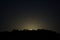 Light of the full moon illuminates the silhouette of evergreen trees along a mountain ridge in the Rockies