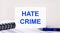 On a light gray background, a notebook, a blue pen and a sheet of paper with the text HATE CRIME. Business concept