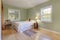Light green walls bedroom interior with two windows and light hardwood floor with white bed and antique chair and casual rug