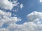 Light Grey and White Multiple Cumulus Fluffy clouds in the Blue Sky behind green leaves from a tree top