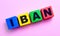 On a light pink background, multi-colored wooden cubes with the text IBAN INTERNATIONAL BANK ACCOUNT NUMBER