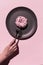 Light pink delicious donat with white marshmallows at the dark grey ceramic plate on the rosy background. Hand of woman