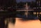 Light reflects fountain discharging water jet on to lake water surface in golden hour twilight. Beautiful Natural Landscape