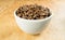 Light roast brown coffee beans in a white bowl on a wooden table top