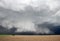 Light shines on a thick shelf cloud hanging low to the ground under a severe storm.