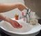 Light-skinned Asian woman rinsing hands in the bathroom sink. Shows hygiene and cleanliness for virus or bacterial spread p