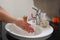 Light-skinned Asian woman rinsing hands in the bathroom sink. Shows hygiene and cleanliness for virus or bacterial spread p