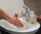 Light-skinned Asian woman rinsing hands in the bathroom sink. Shows hygiene and cleanliness for virus or bacterial spread p