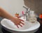 Light-skinned Asian woman rinsing hands in the bathroom sink. Shows hygiene and cleanliness for virus or bacterial spread p