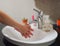 Light-skinned Asian woman rinsing hands in the bathroom sink. Shows hygiene and cleanliness for virus or bacterial spread p