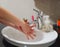 Light-skinned Asian woman rinsing hands in the bathroom sink. Shows hygiene and cleanliness for virus or bacterial spread p