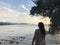 A light-skinned brown-haired girl in light beach clothes sits on the stones of the coastline of Karon beach in Phuket in Thailand