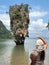 A light-skinned girl in beach clothes stands with her back to the camera and looks at the famous picturesque James bond island in