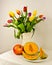 A light still life with a bouquet of colourful tulips and fruits, a melon and a pomegranate