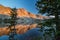 The light of sunrise reflects an image of the mountains off the still surface of a lake.