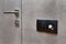 Light switch on the gray textured wall next to the door with metallic handle.