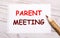 On a light wooden background, a colored pencil and a white sheet of paper with the text PARENT MEETING