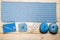 On light wooden background is fragment of crocheted napkin with decorative elements, knitting accessories, blue balls of yarn