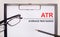 On a light wooden background glasses, a pen and a sheet of paper with the text ATR Average True Range. Business concept
