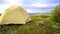 Light yellow tent sways in strong wind at beautiful morning mountain landscape