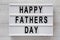 Lightbox with `Happy Fathers Day` words over white wooden background, top view. Overhead, from above, flat lay. Close-up