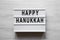 Lightbox with `Happy Hanukkah` word over white wooden background, overhead view. From above, flat-lay