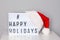 Lightbox with happy holidays hashtag text and red Santa hat on white table