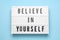 Lightbox with motivational quote Believe in Yourself on light blue background, top view