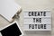 Lightbox with text `Create the future`, clipboard with sheet of paper on a white wooden surface, top view. From above, flat lay,