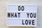 Lightbox with text `Do what you love` over white wooden surface, top view. From above, flat lay,