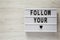 Lightbox with text `Follow you heart` over white wooden surface. Copy space