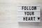 Lightbox with text `Follow your heart` on a white wooden surface, top view. Flat lay, overhead. Copy space. Valentine`s Day 14