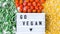Lightbox with text GO VEGAN frozen vegetables food of yellow corn, green beans, red tomatoes. Colors of traffic light. Harvest