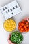 Lightbox with text GO VEGAN Three Bowls of frozen vegetables food of yellow corn, green beans, red tomatoes. Colors of traffic