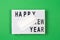 Lightbox with text HAPPY NEW YEAR and medical mask on green background. Top view